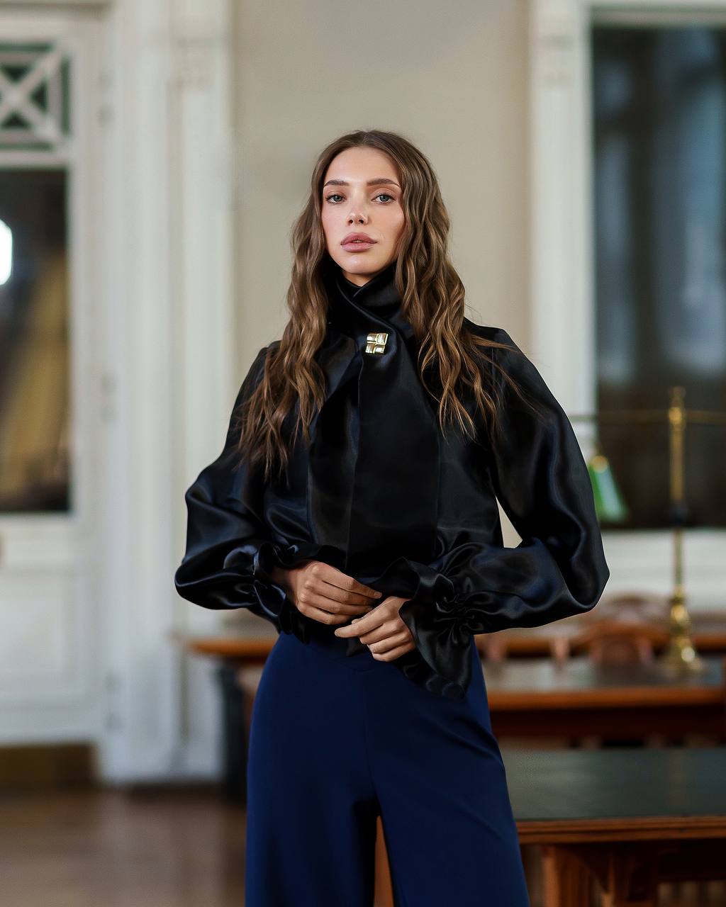 Woman wearing a black blouse with puffed sleeves and blue pants in an indoor setting.