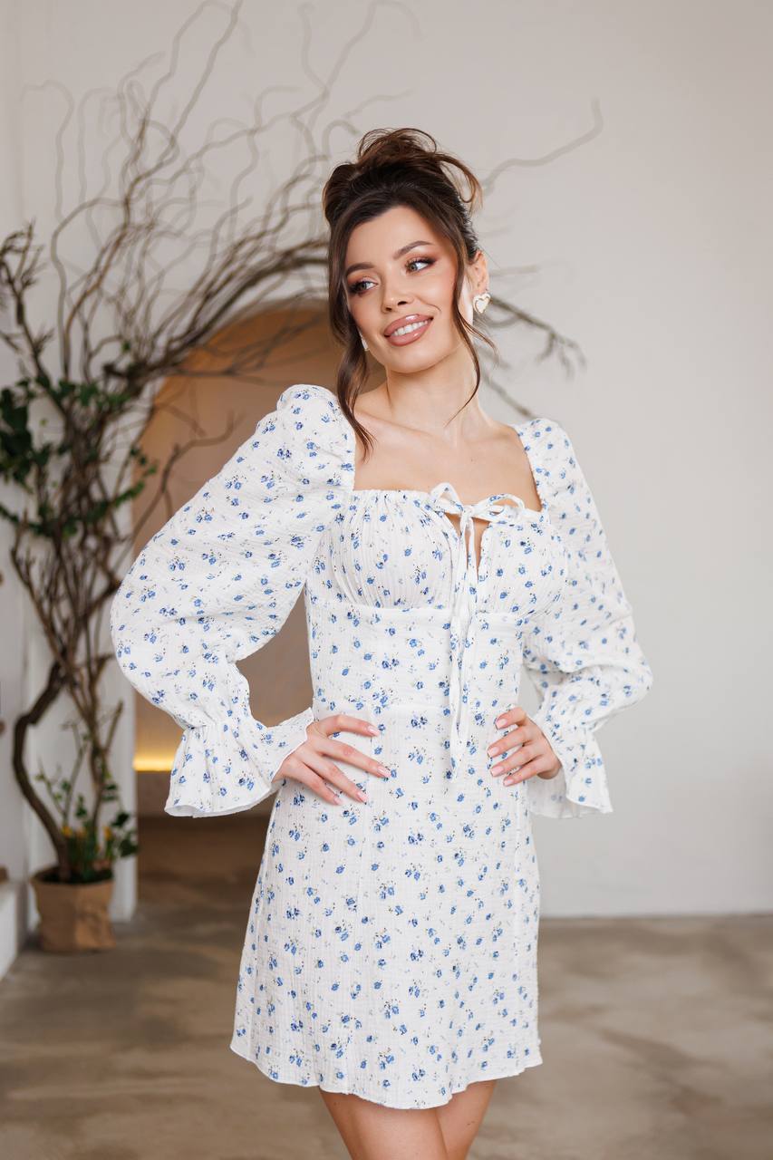 Woman wearing a white floral dress in an indoor setting with a plant in the background