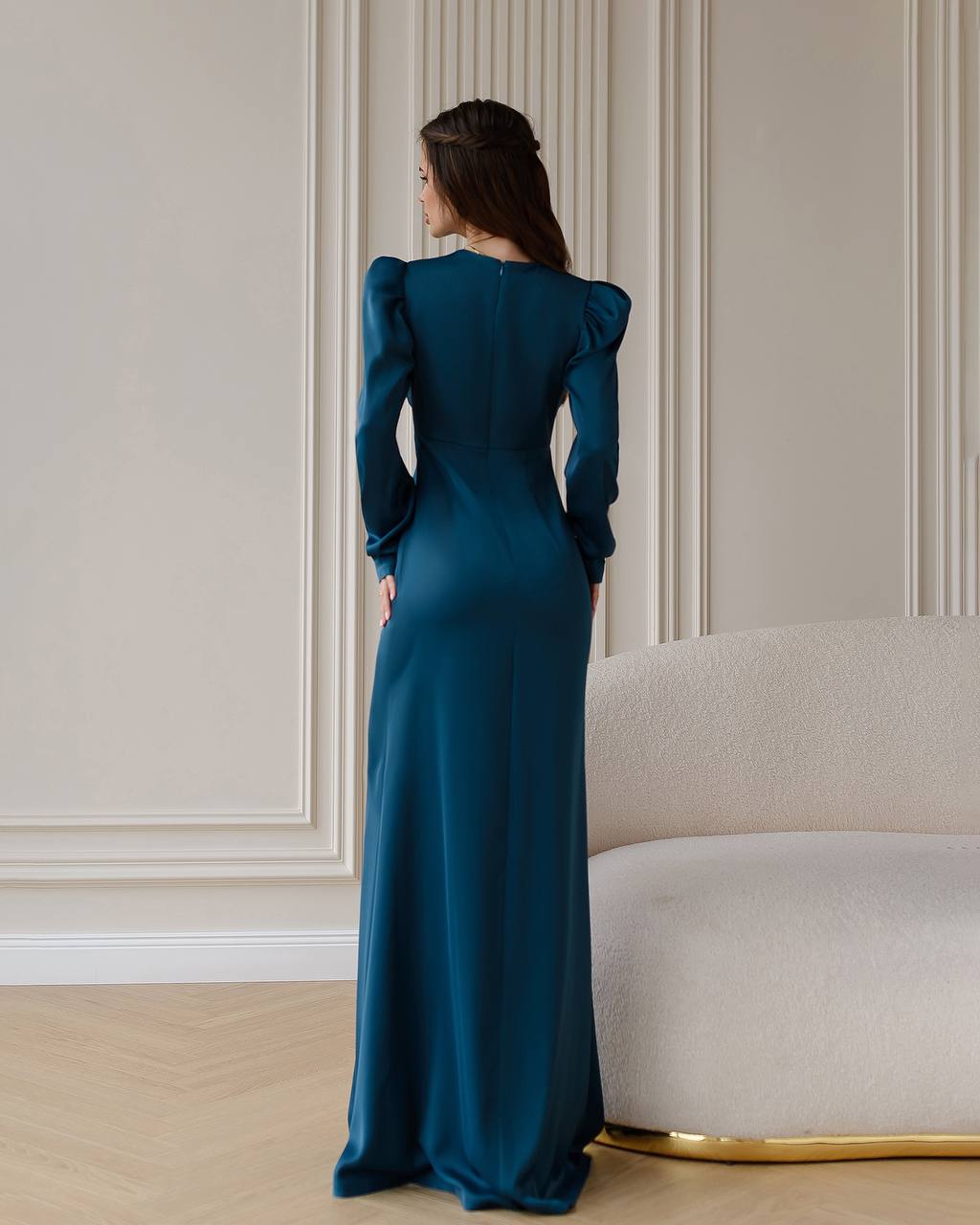 Woman in a teal evening gown standing in a room with a neutral color scheme.