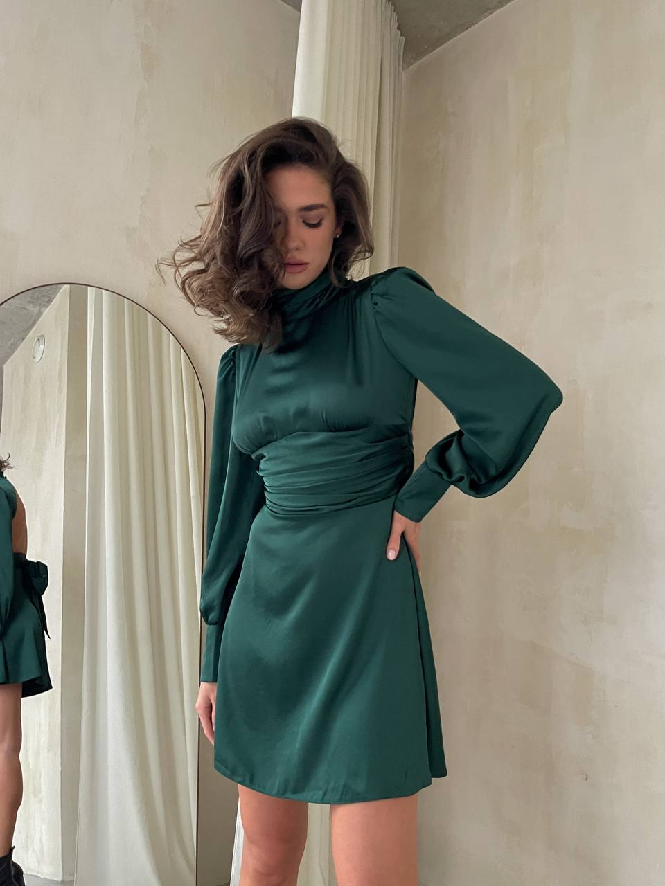 Woman wearing a green dress standing in front of a mirror.