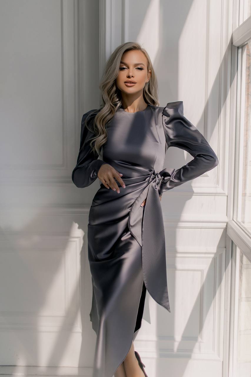 Woman in a gray satin dress standing in a bright room with large windows.