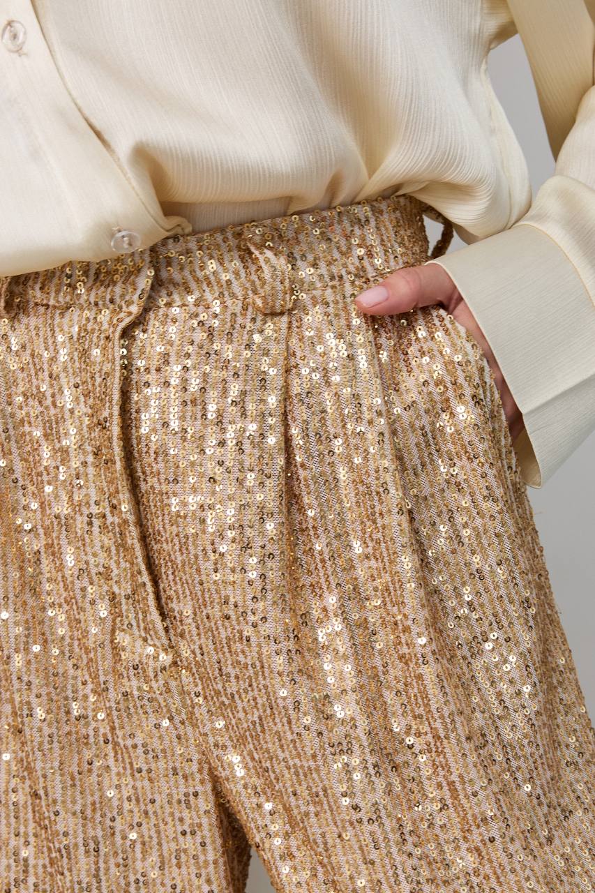 Close-up of gold sequin pants with a beige blouse.