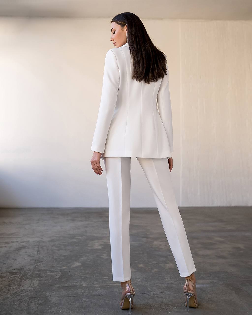 Woman wearing a white suit standing in a minimalistic room.