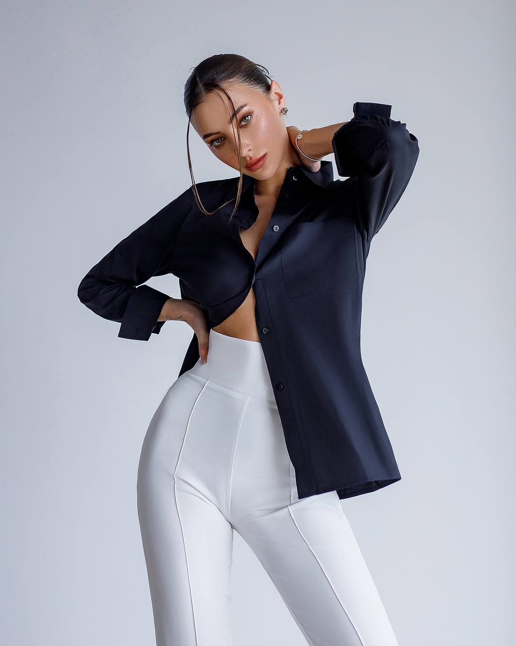 Woman wearing a black shirt and white pants on a gray background