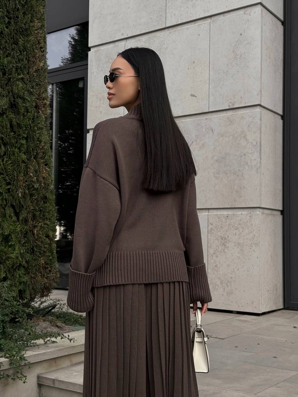 Woman in a brown outfit standing against a light stone building.