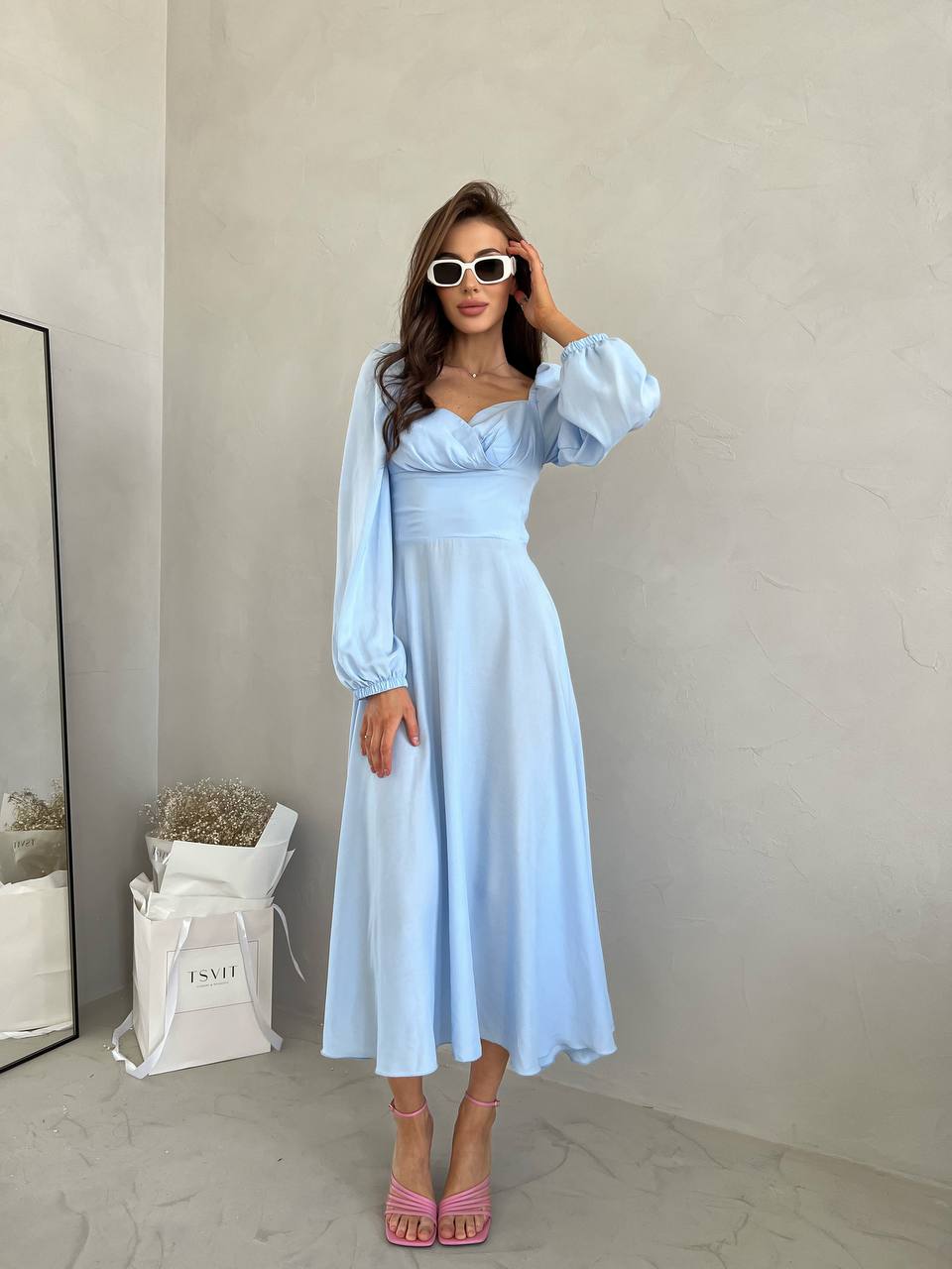 Woman wearing a light blue dress with long sleeves in a minimal indoor setting.