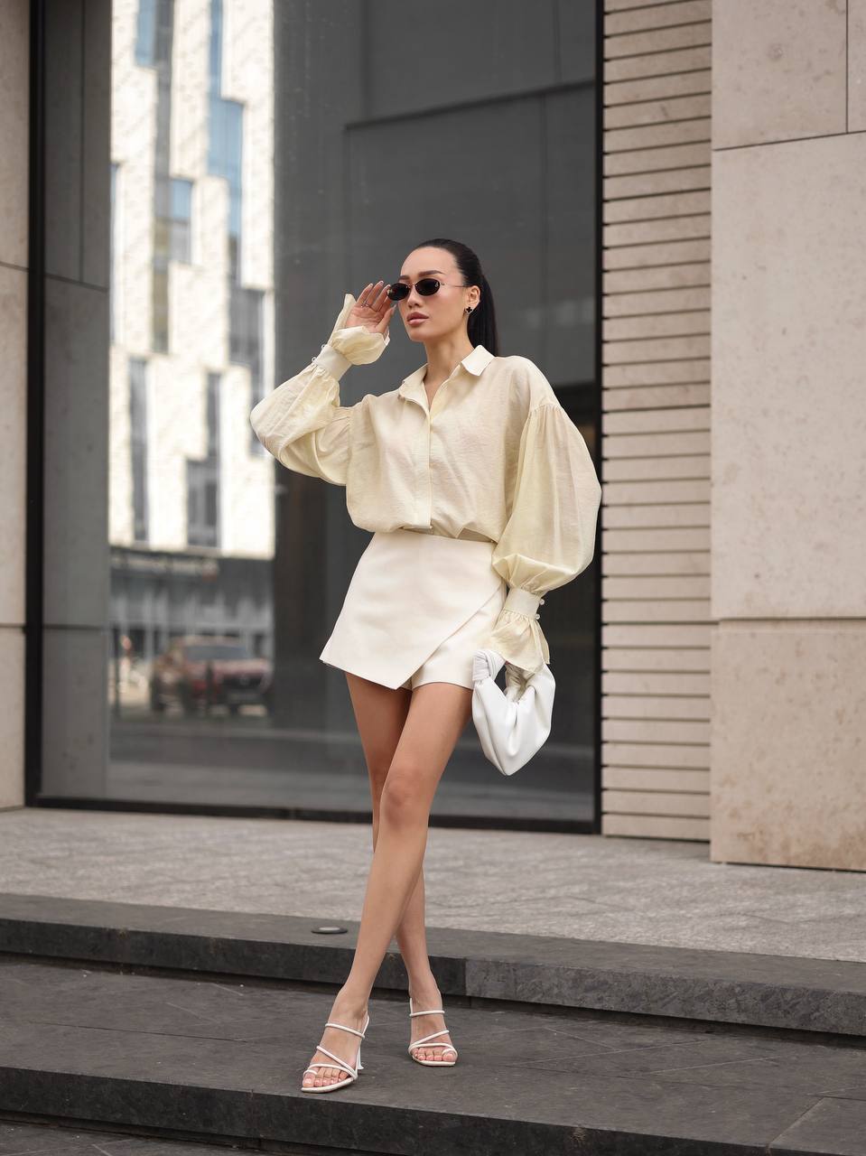 Woman in a light-colored outfit standing outdoors with modern architecture in the background