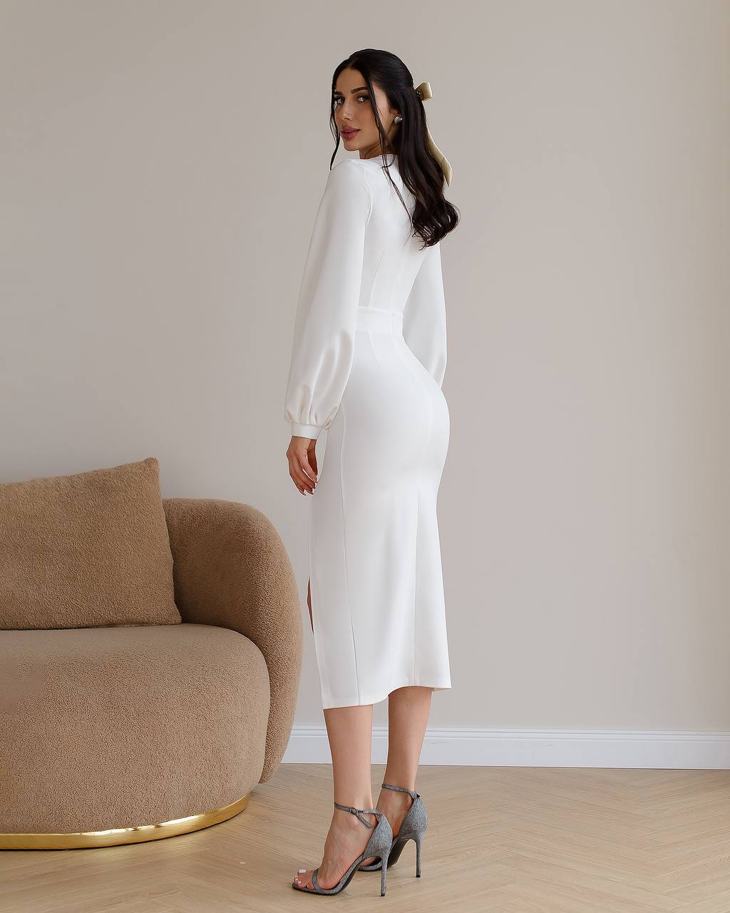 Woman in a white dress standing in a room with a beige sofa.