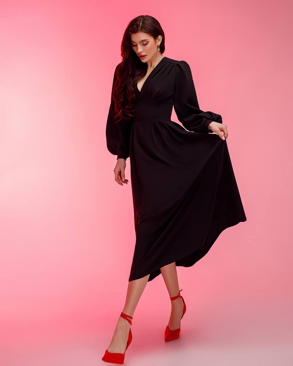 Woman wearing a black dress with red shoes on a pink background