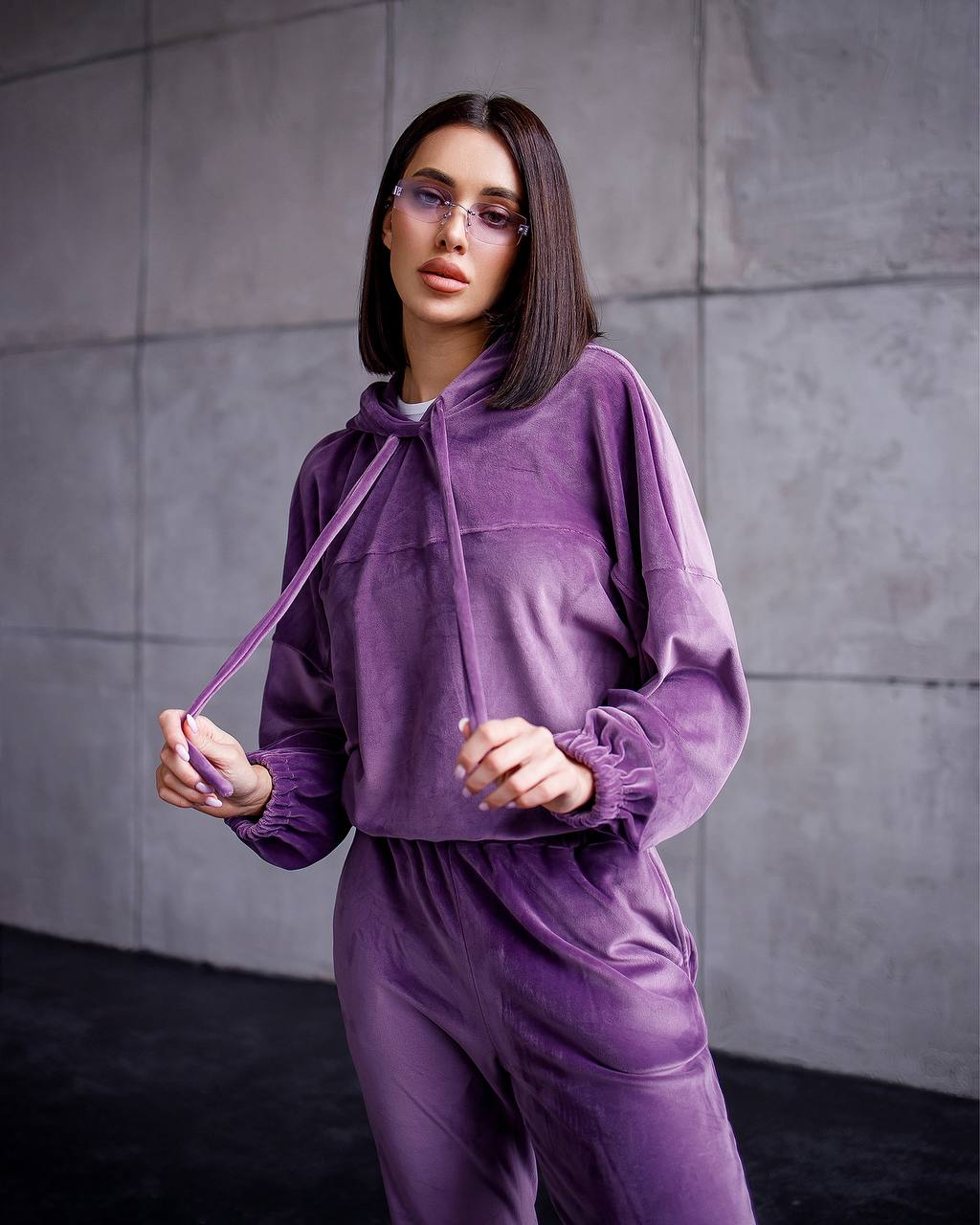 Person wearing a purple tracksuit against a gray tiled wall.