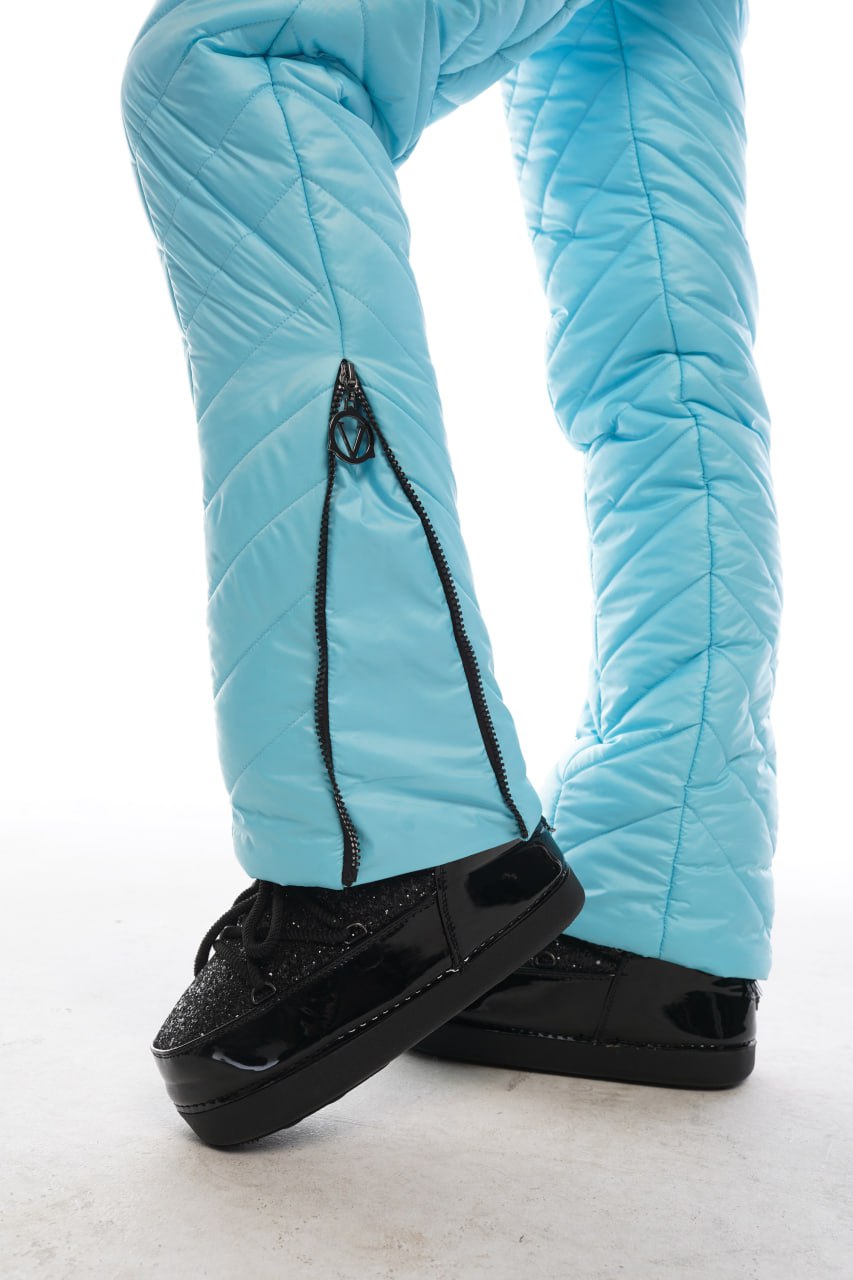 Light blue quilted pants with black ski boots on a white background