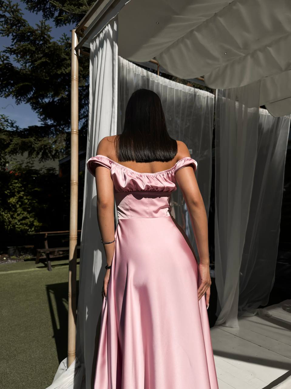 Woman in a pink off-shoulder dress standing outdoors with white curtains in the background