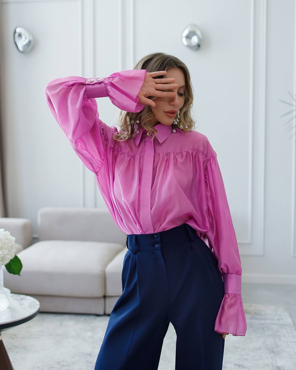Person wearing a pink blouse and blue pants in a room with white walls and a sofa.