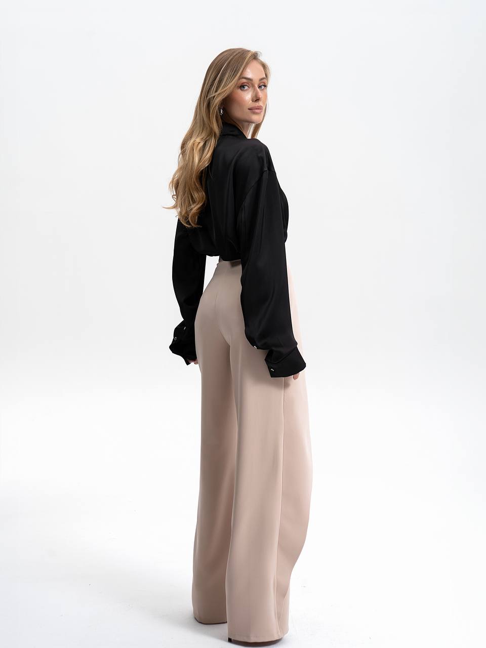 Woman wearing a black top and beige pants on a white background