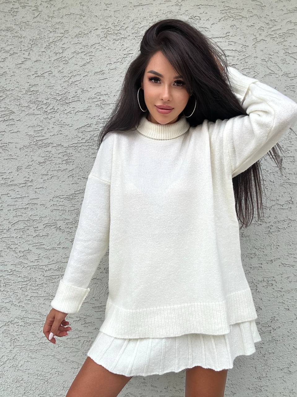 Woman wearing a white sweater and skirt against a gray wall