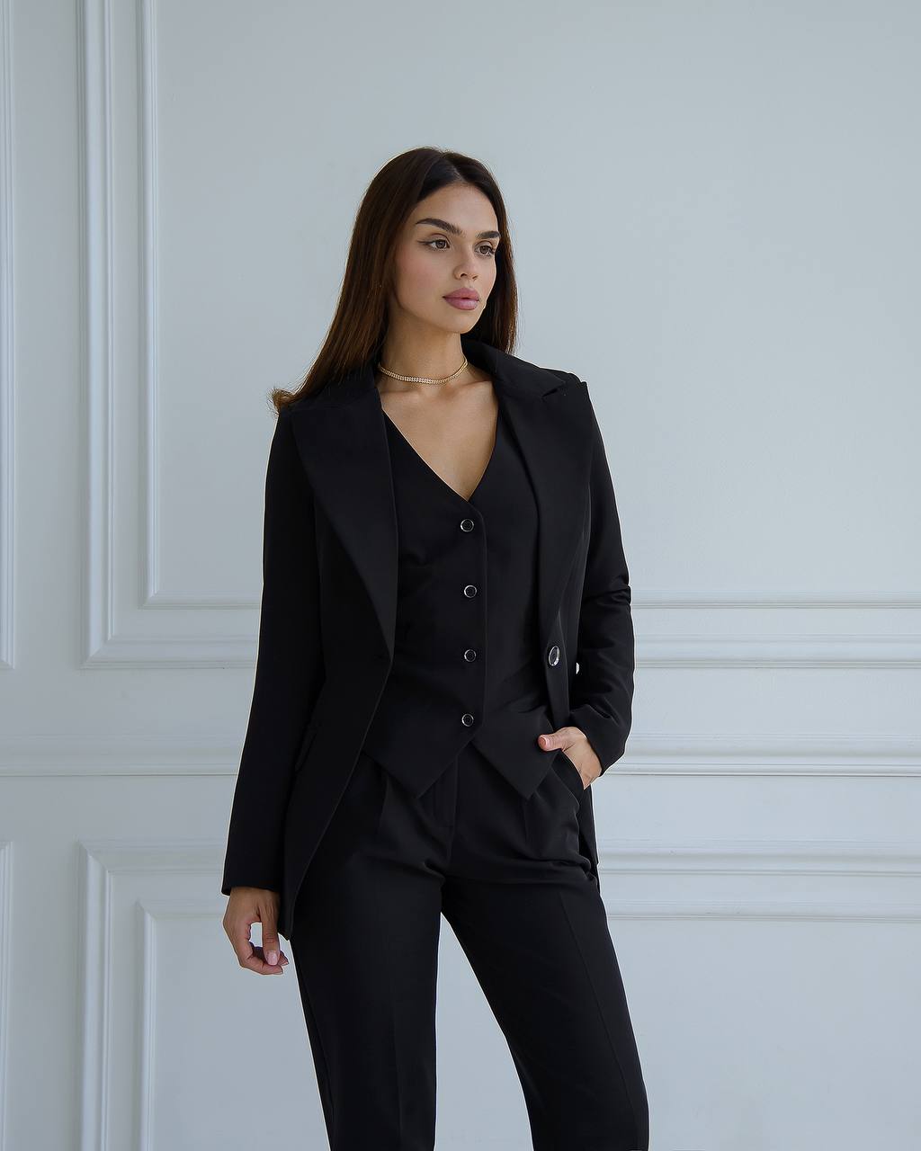 Woman wearing a black suit standing against a white paneled wall