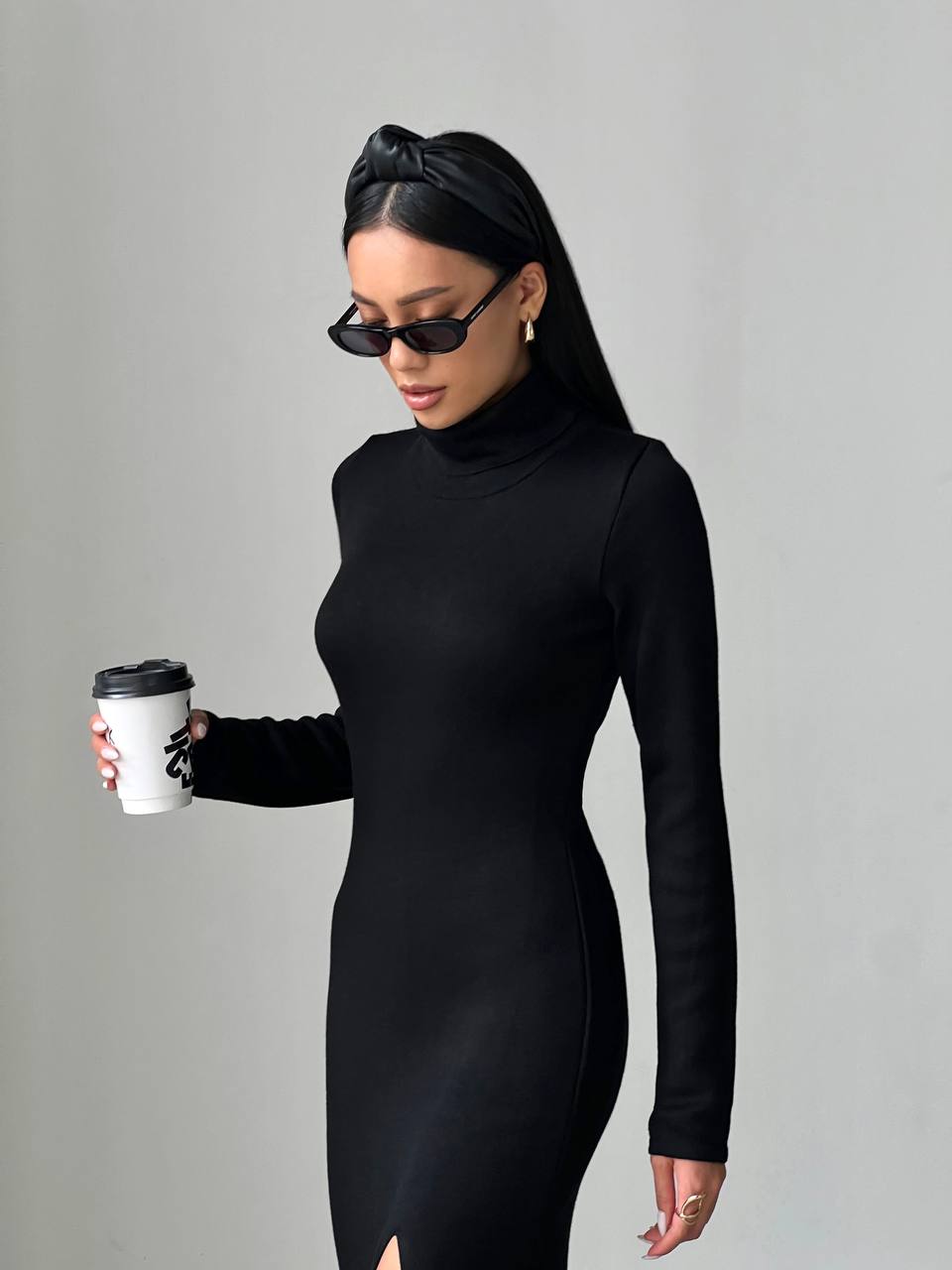 Woman in a black dress holding a coffee cup against a gray background