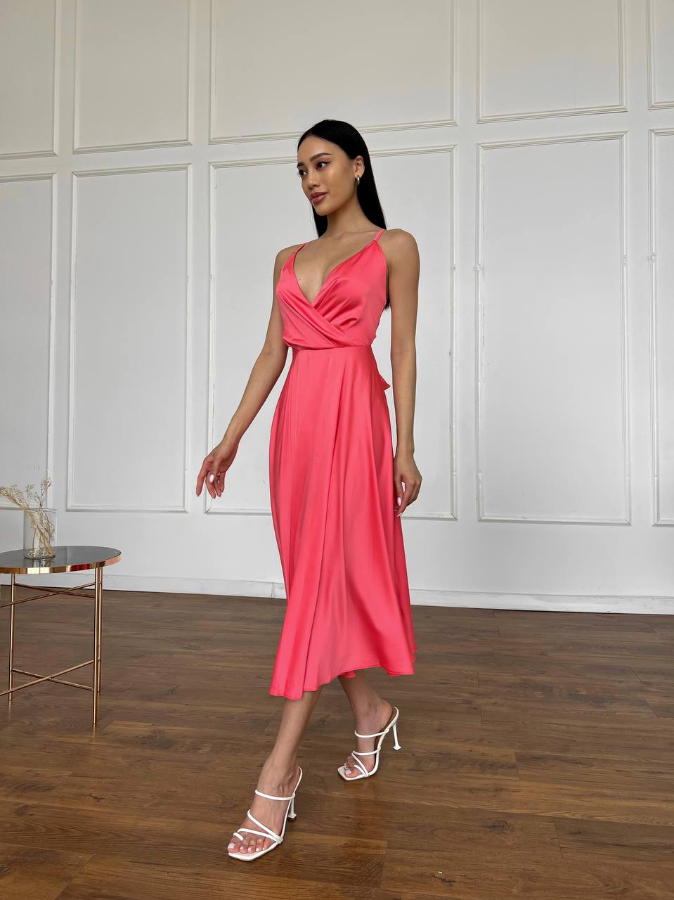 Woman in a pink dress standing in a room with wooden flooring and white paneled walls.