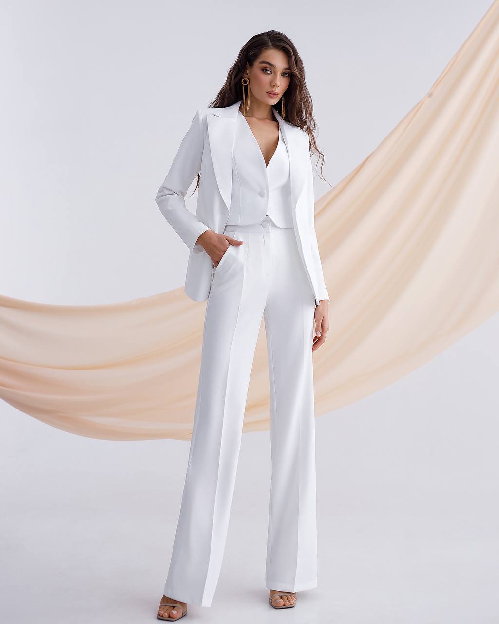 Woman wearing a white suit with a beige drape in the background