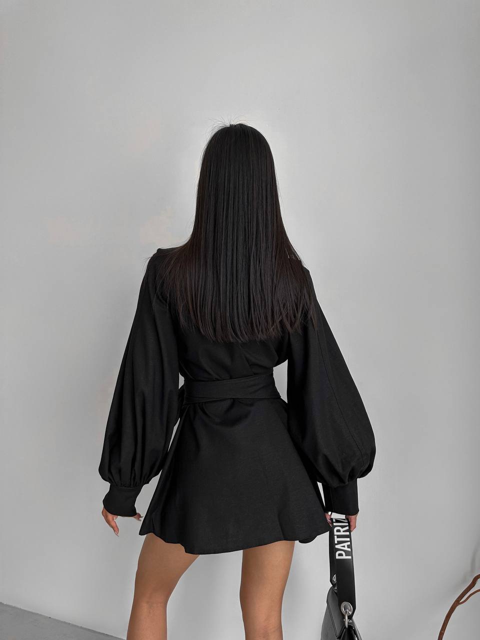 Person wearing a black dress with long sleeves against a plain background