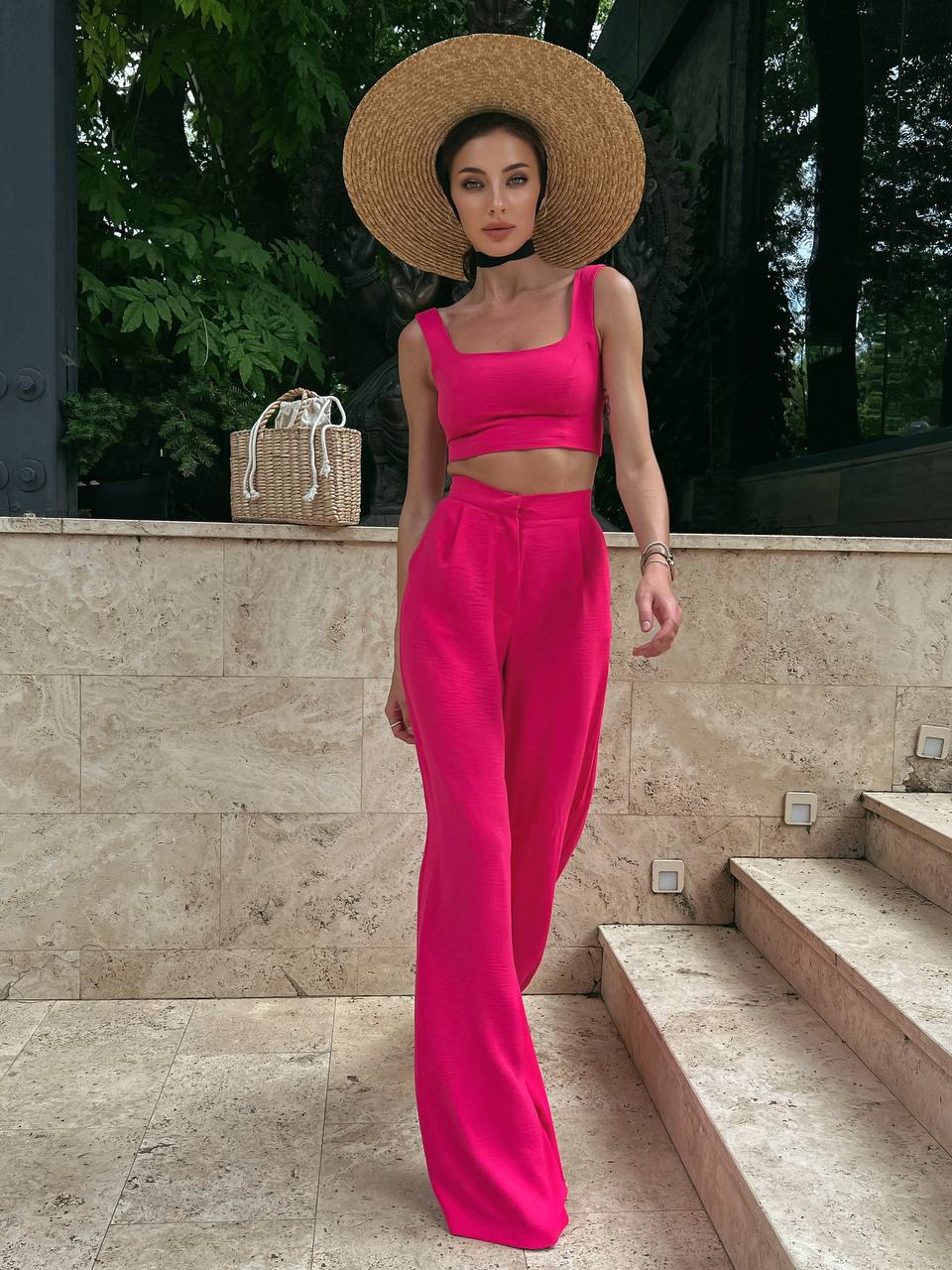 Woman in bright pink outfit with straw hat standing outdoors.