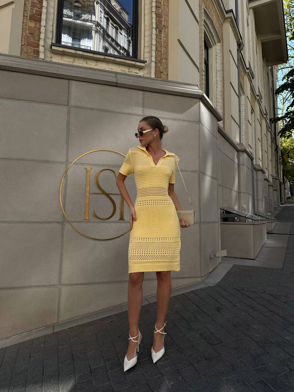 Woman in a yellow dress standing in front of a building with a logo.