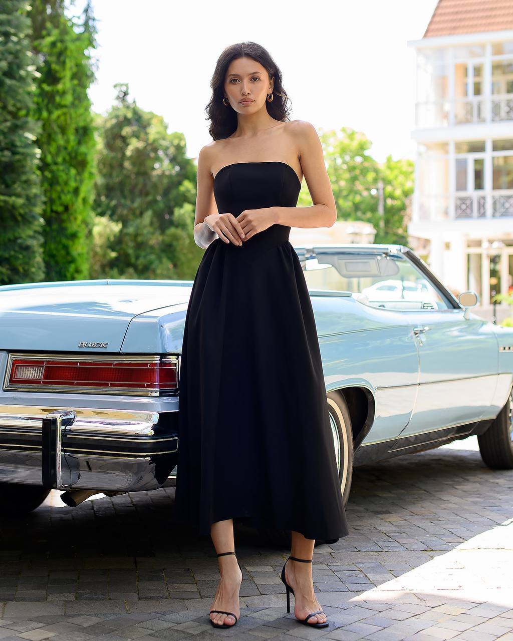 Woman in a black strapless dress standing in front of a vintage car.