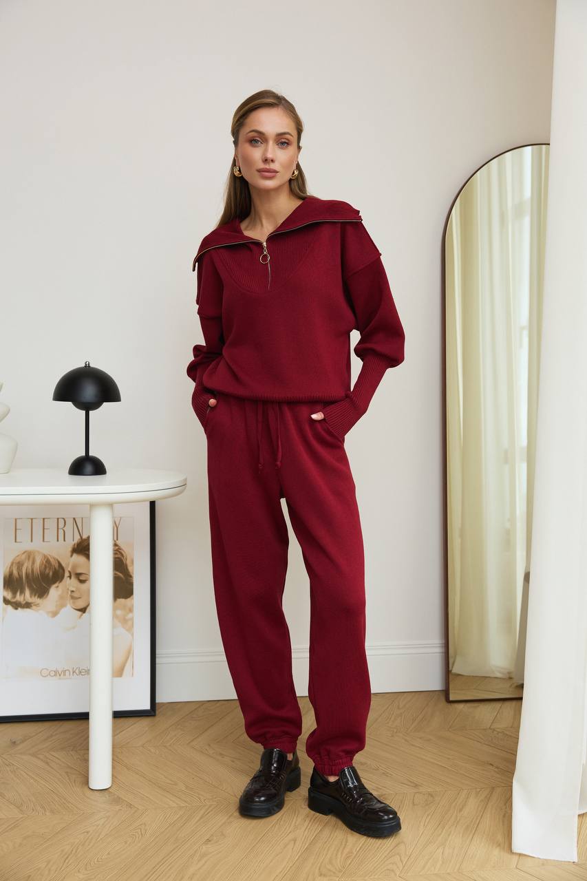 Woman wearing a red tracksuit standing in a room with a mirror and table.