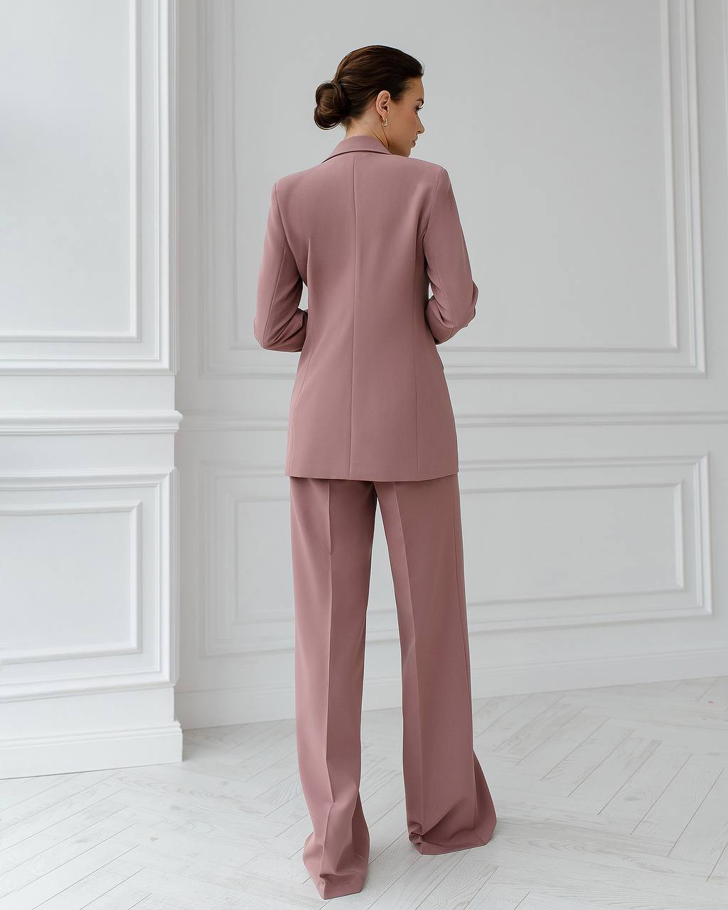Woman wearing a pink suit standing in a room with white paneled walls.