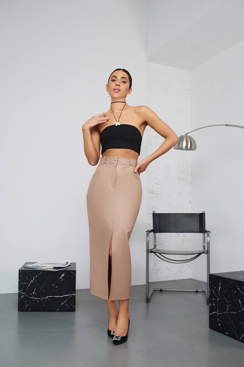 Woman wearing a black top and beige skirt in a minimalistic room.