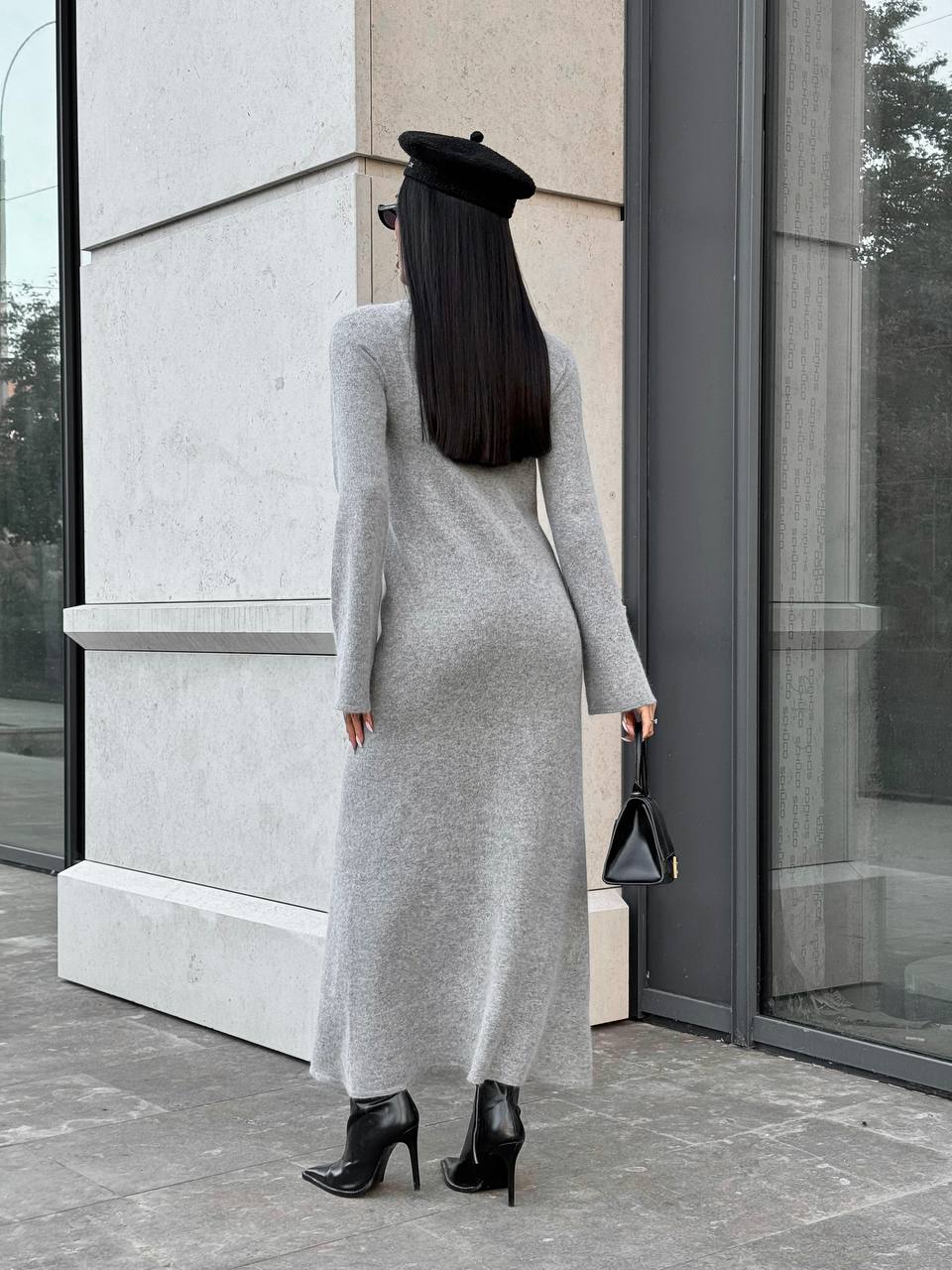 Woman in a long gray dress standing outside a modern building.