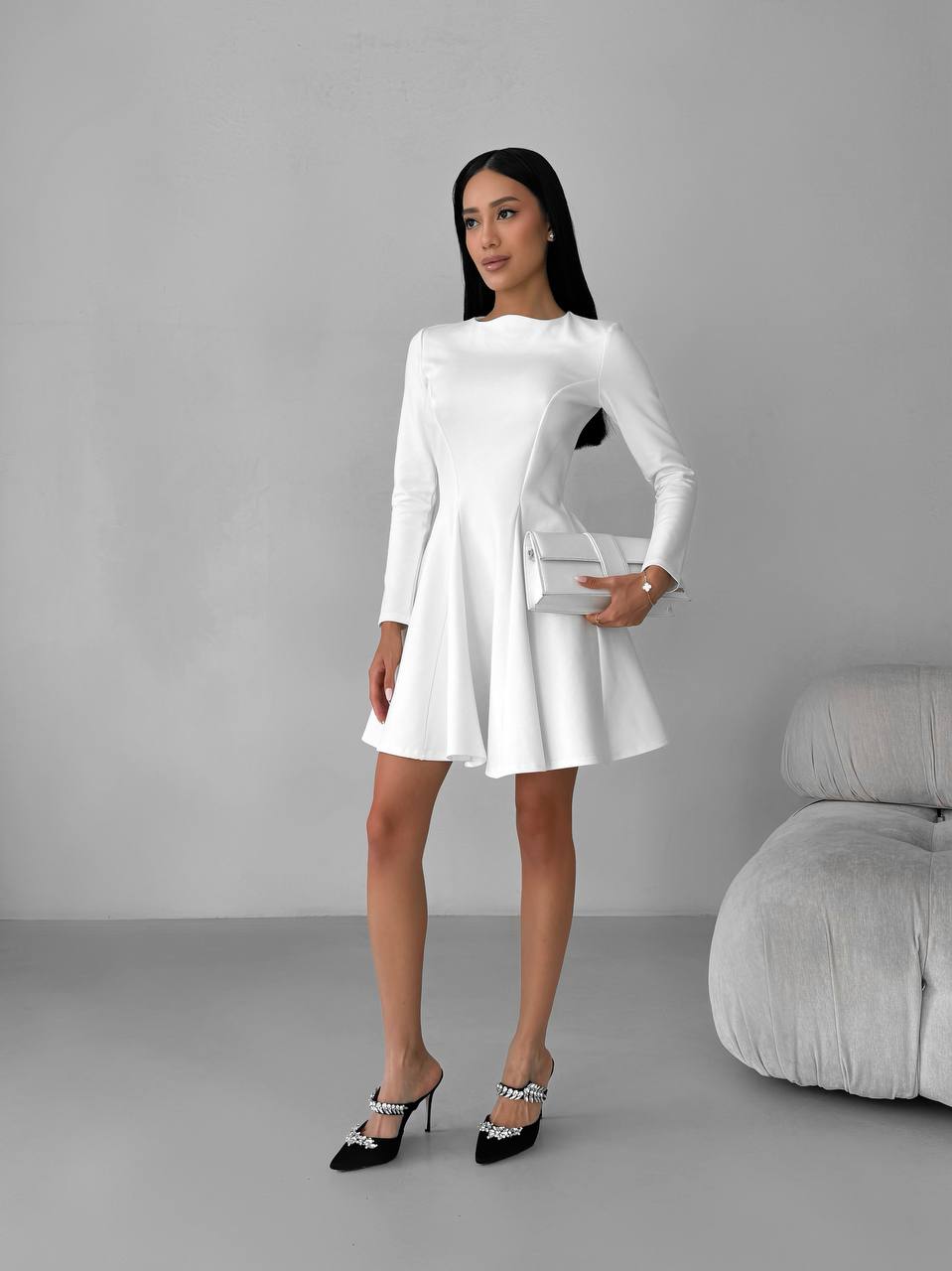 Woman in a white dress holding a clutch against a gray background