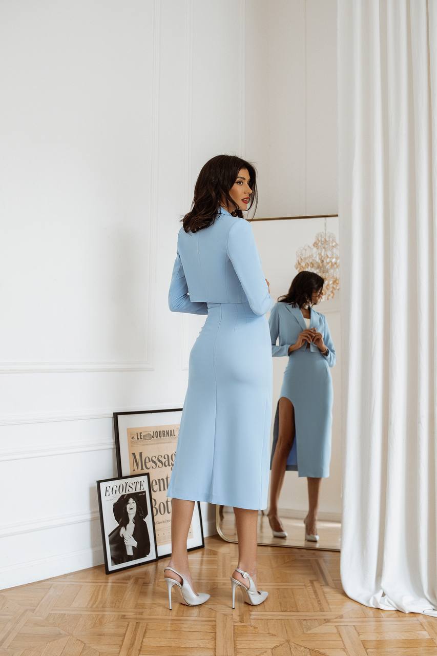 Woman in a light blue dress standing in front of a mirror in a room with decor elements.