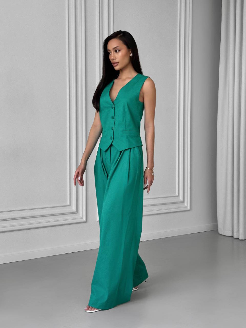 Woman wearing a green jumpsuit standing against a gray wall.