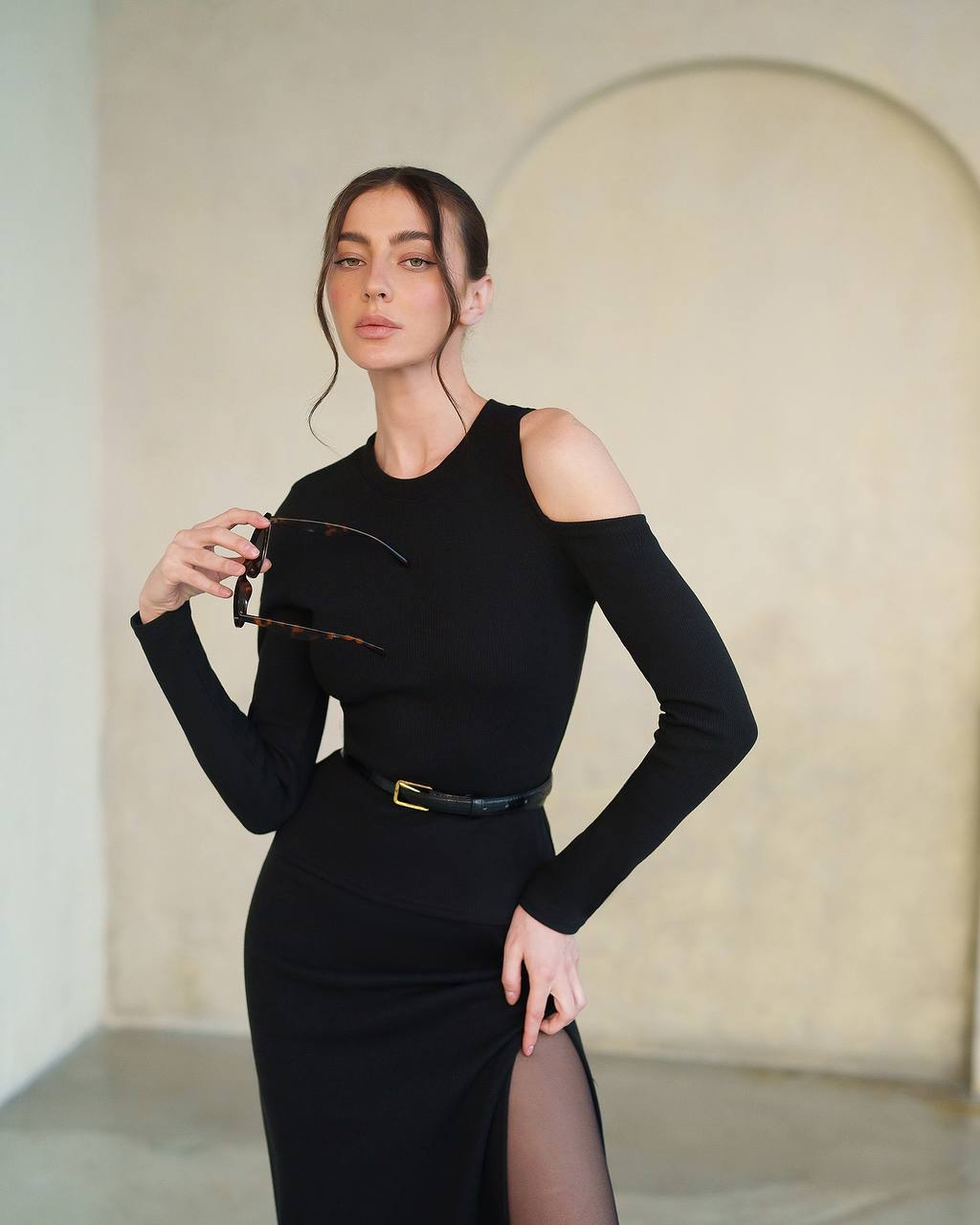 Woman wearing a black outfit with sheer sleeves against a neutral background