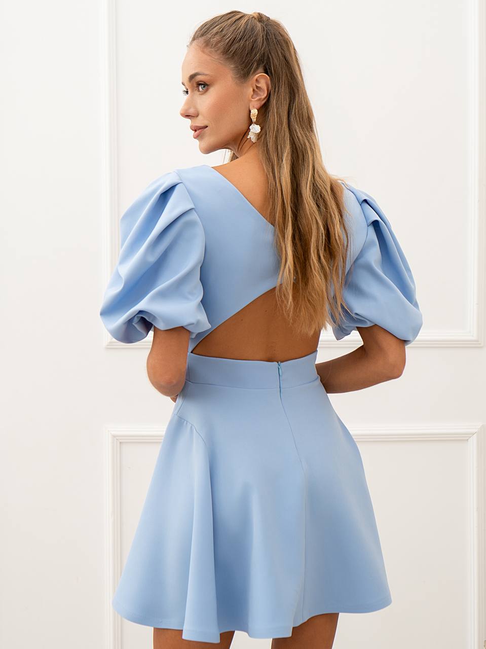 Woman wearing a light blue dress with puffed sleeves and open back against a white background