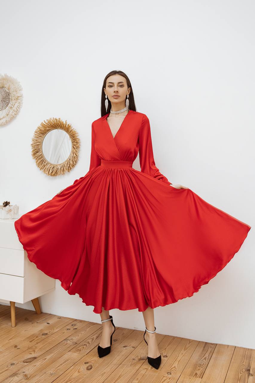 Woman wearing a red dress standing in a room with wooden floor and white walls.