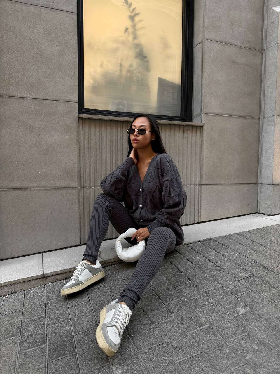 Person sitting on a sidewalk wearing sunglasses and casual clothing.