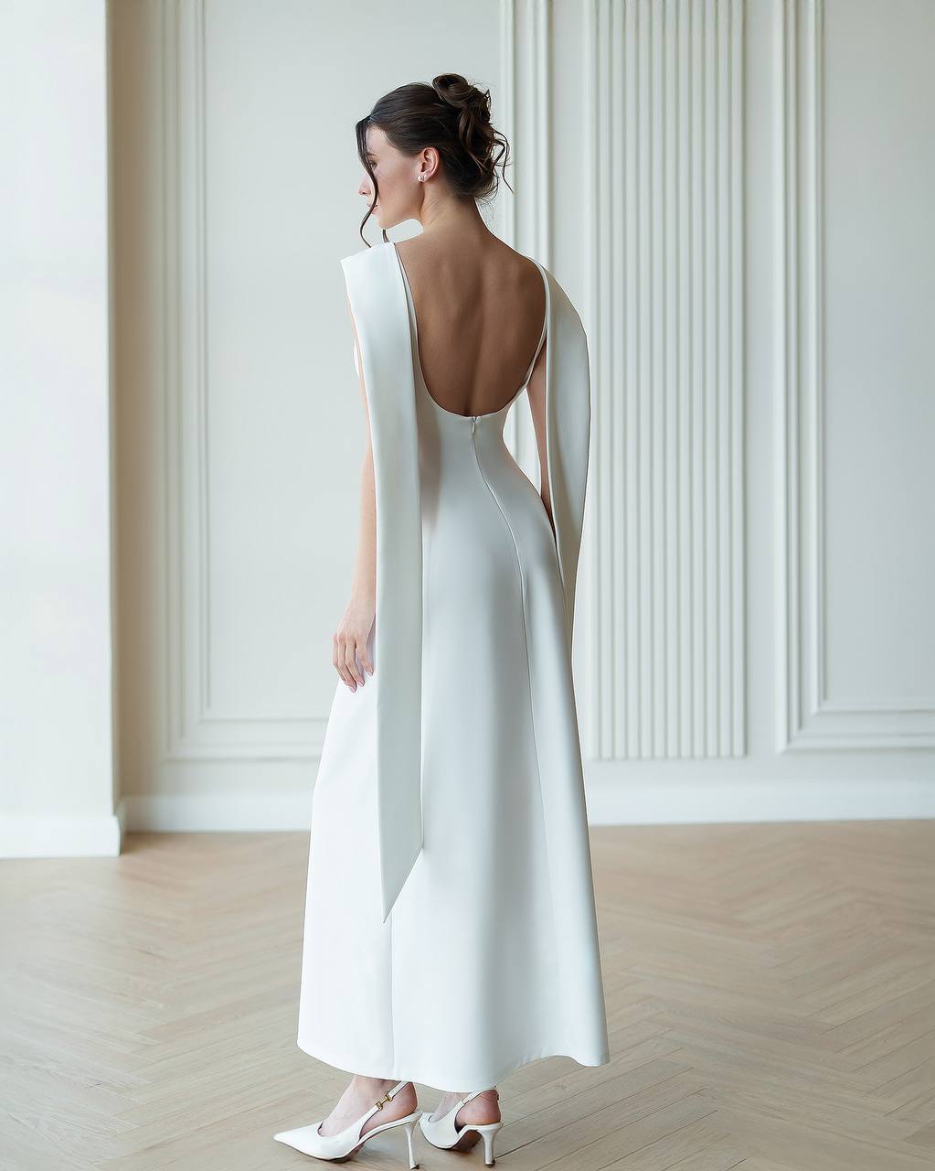 Woman wearing a white dress with a backless design in a minimalistic setting.