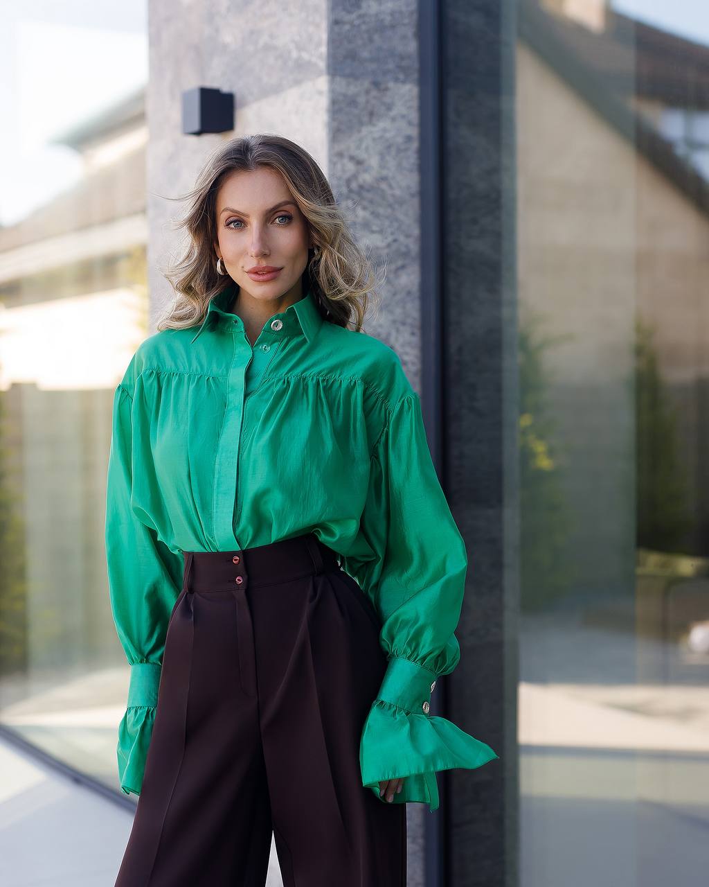 Woman wearing a green blouse and dark pants standing in front of a modern building.