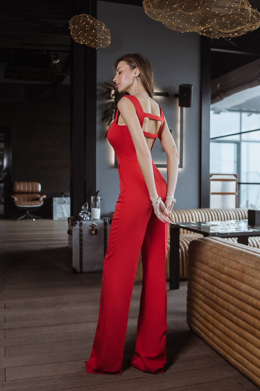 Woman in a red jumpsuit standing in an elegant interior setting