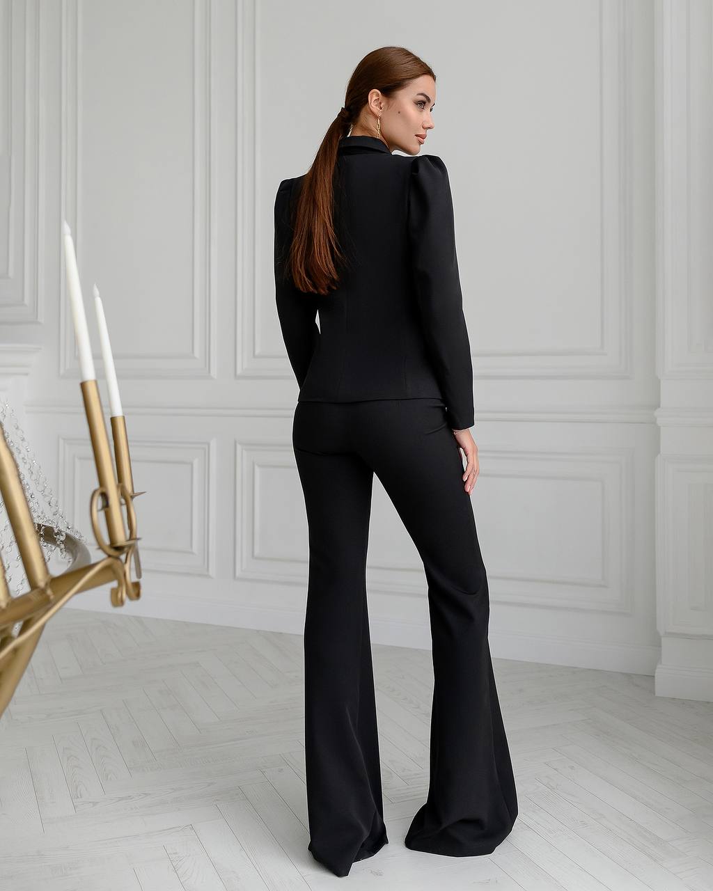 Woman wearing a black outfit in a room with white walls and a gold candlestick.