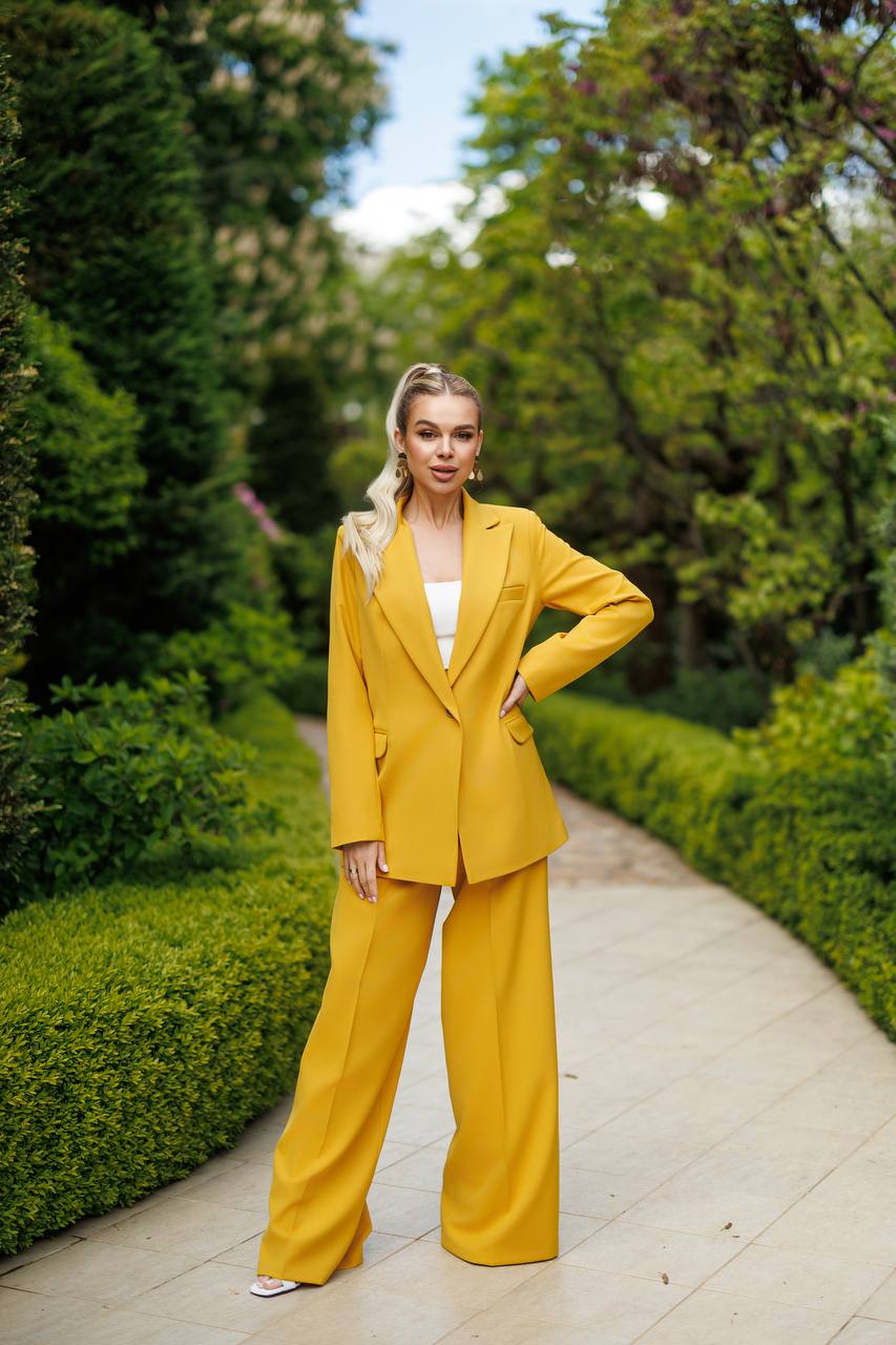 Woman in a yellow suit standing on a path with greenery around