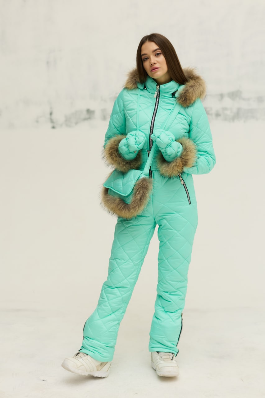 Person wearing a teal winter suit with fur trim on a light background