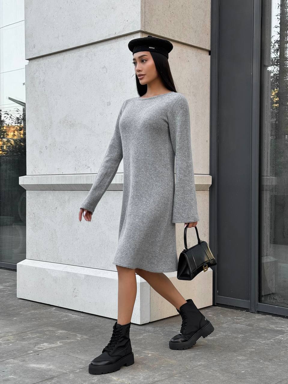 Woman in a gray dress and black boots standing outside a building.