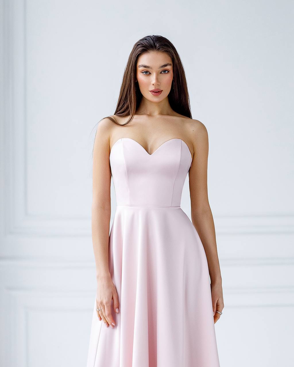 Woman wearing a light pink strapless dress against a white background