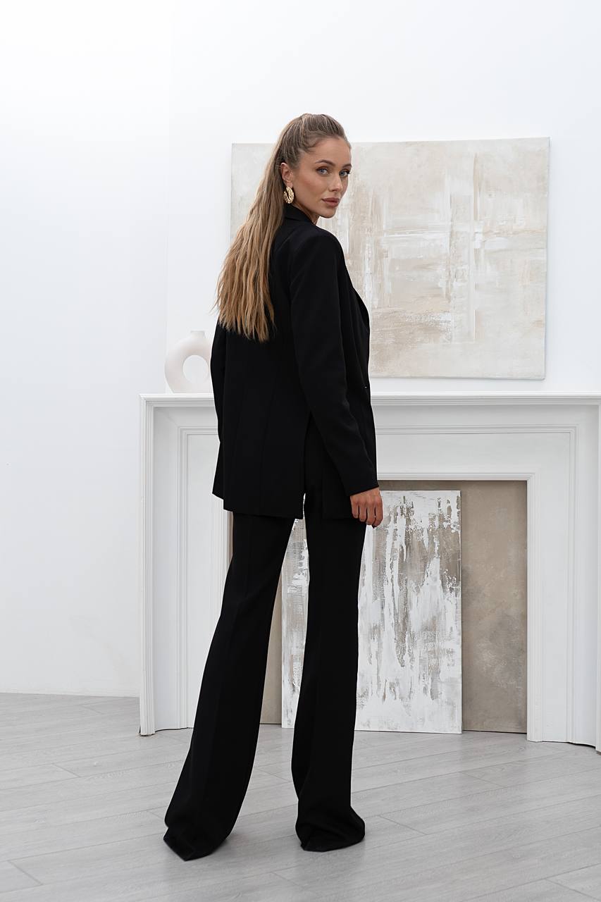 Woman in a black suit standing in a room with abstract art on the wall.