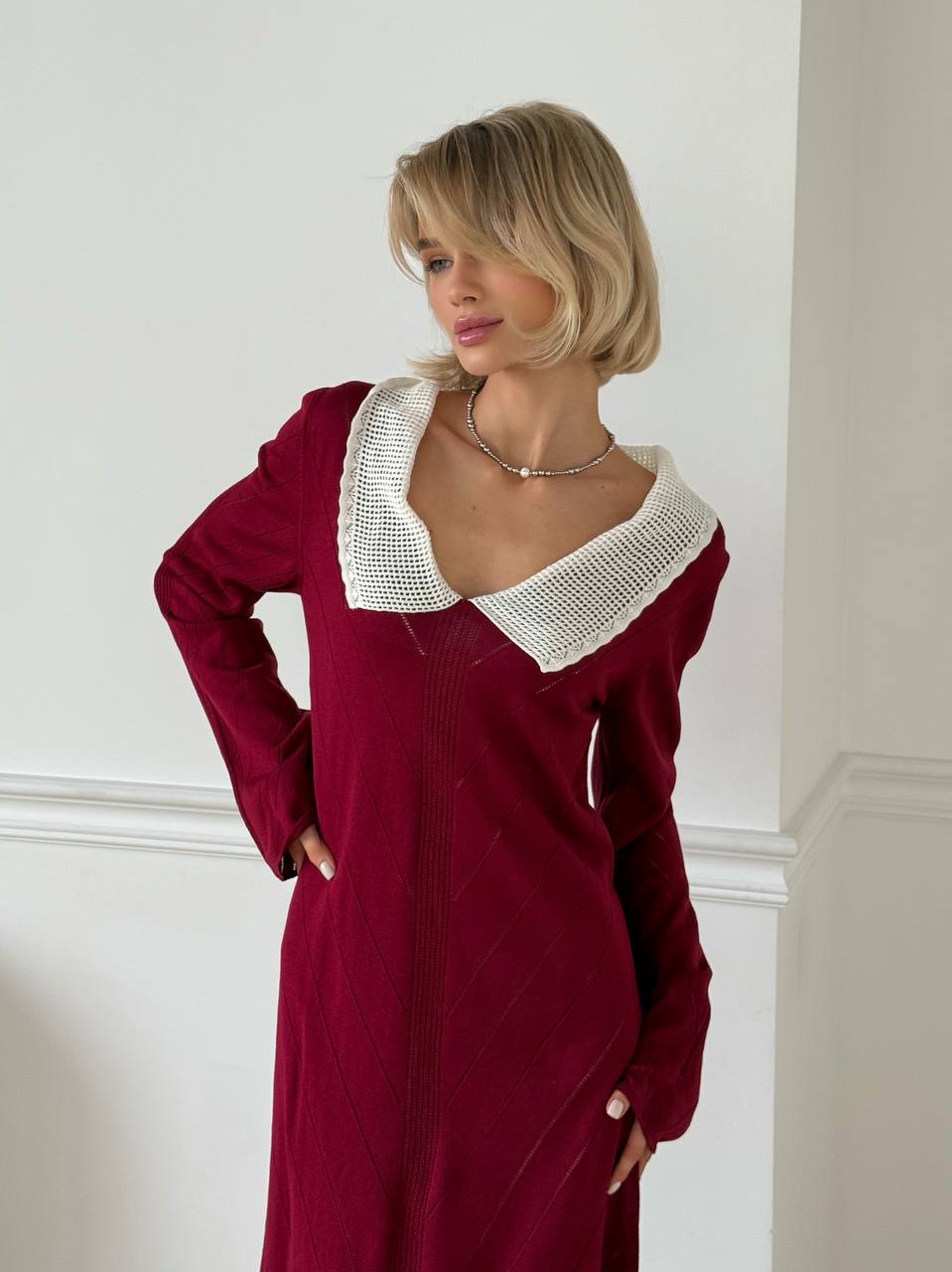 Woman wearing a burgundy dress with a white collar against a plain background