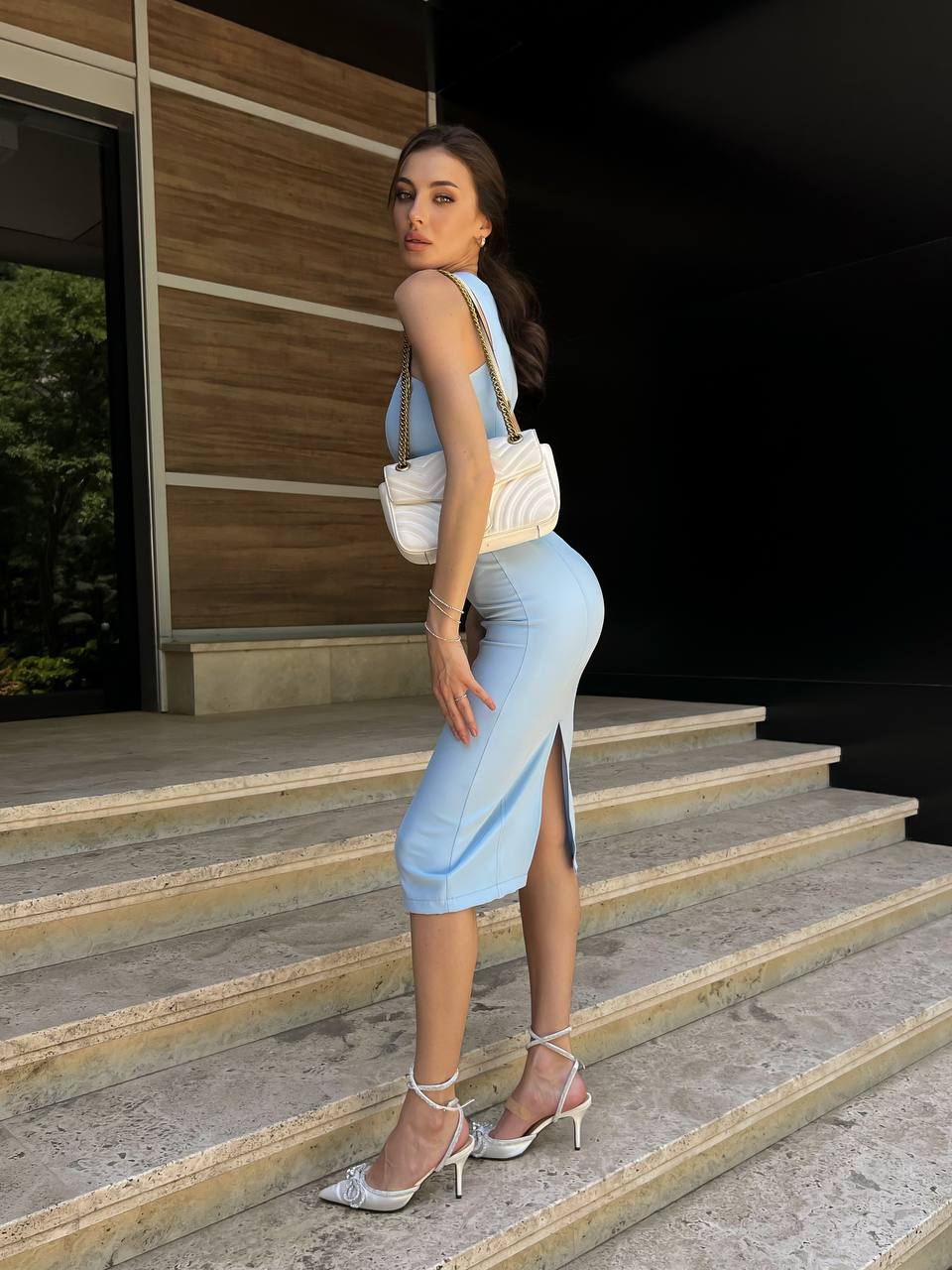Woman in light blue outfit standing on steps with a neutral background
