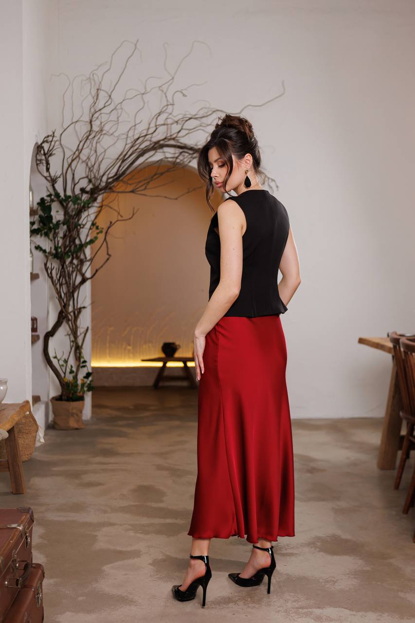 Woman in a black top and red skirt standing in a room with minimal decor.